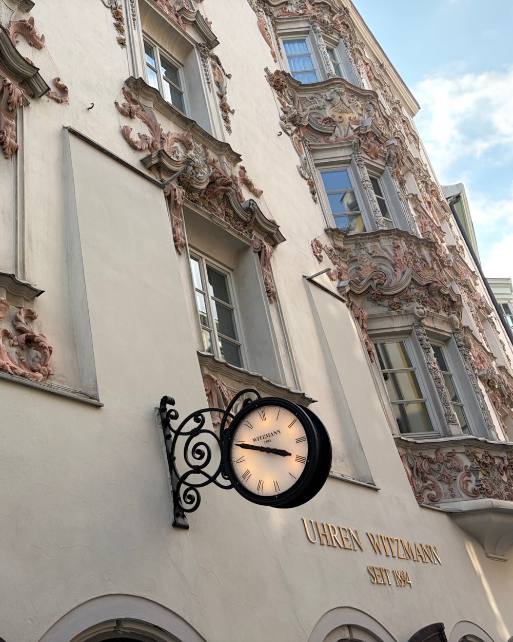 A baroque facade in Innsbruck with a hanging clock above a watchmaker shop sign