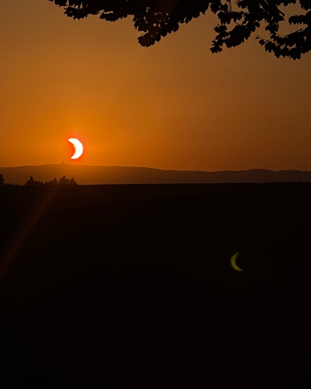 A partial solar eclipse at sunset over dark fields