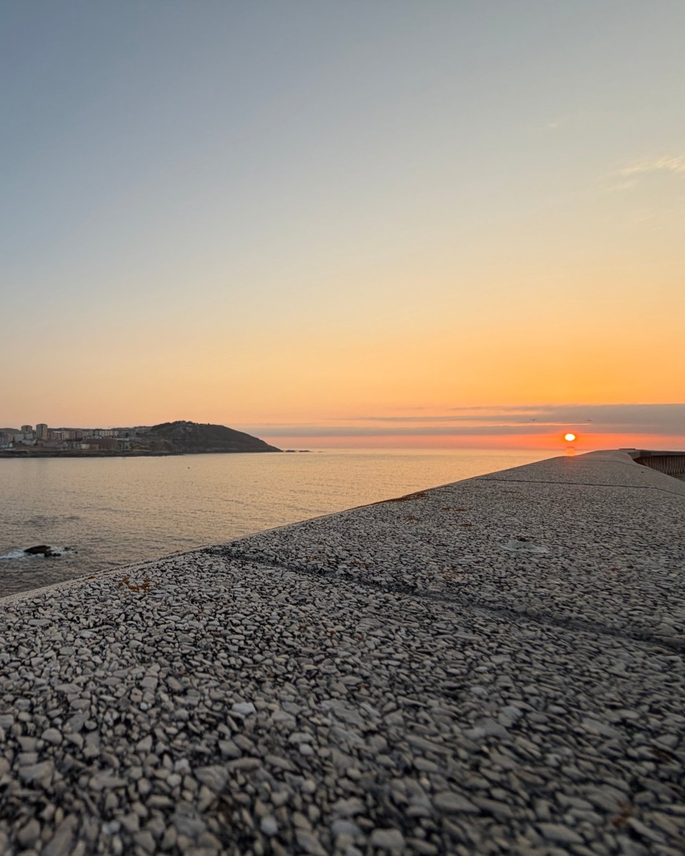 The sun setting over a calm sea, seen along a stone sea wall