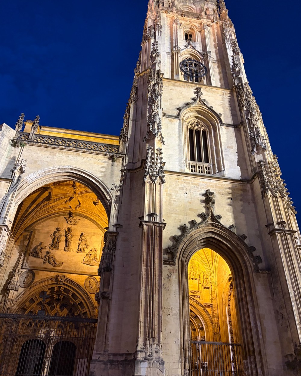 A floodlit Gothic cathedral tower and arched portals against a deep blue night sky